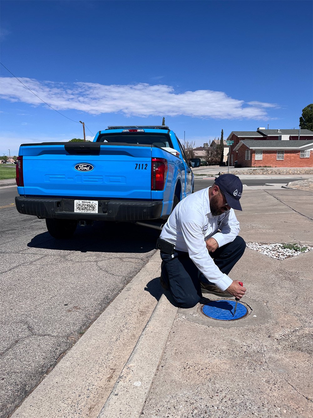 Worker examining manhole beside blue truck